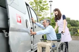 スタッフにサポートされながら介護タクシーに乗り込む車椅子の男性