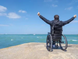 車椅子の男性が海に向かって両腕を広げている
